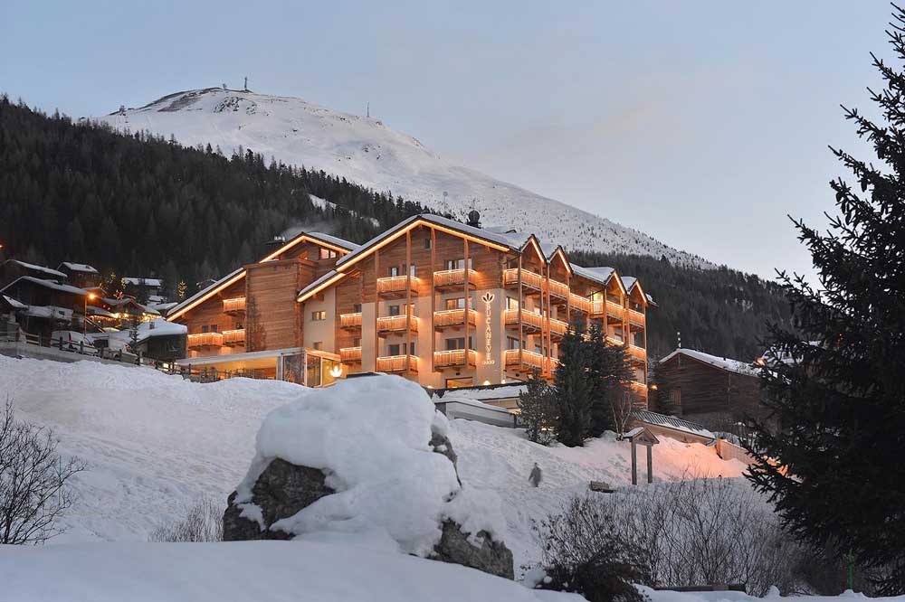 Hotel di montagna illuminato al tramonto con neve circostante.